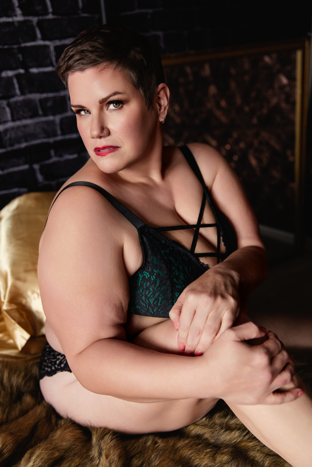 A person in a green lace bra and black lace underwear sits on a fur blanket holding a knee after shopping for lingerie in indianapolis