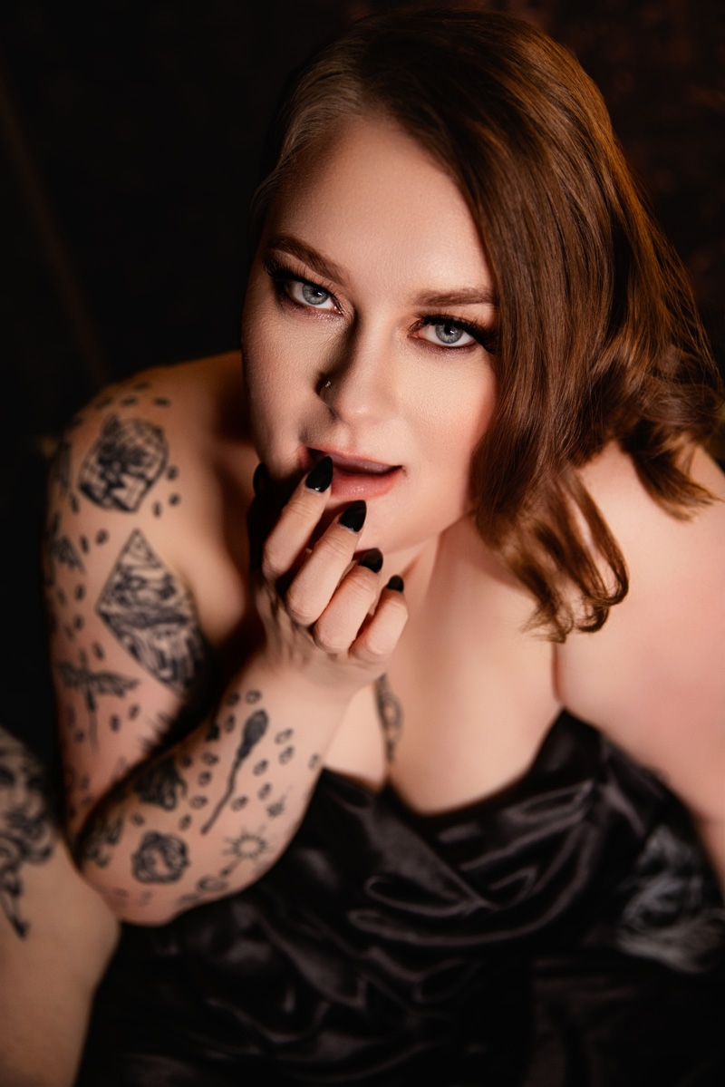 A woman rests her finger on her lip while wrapped in a silk blanket