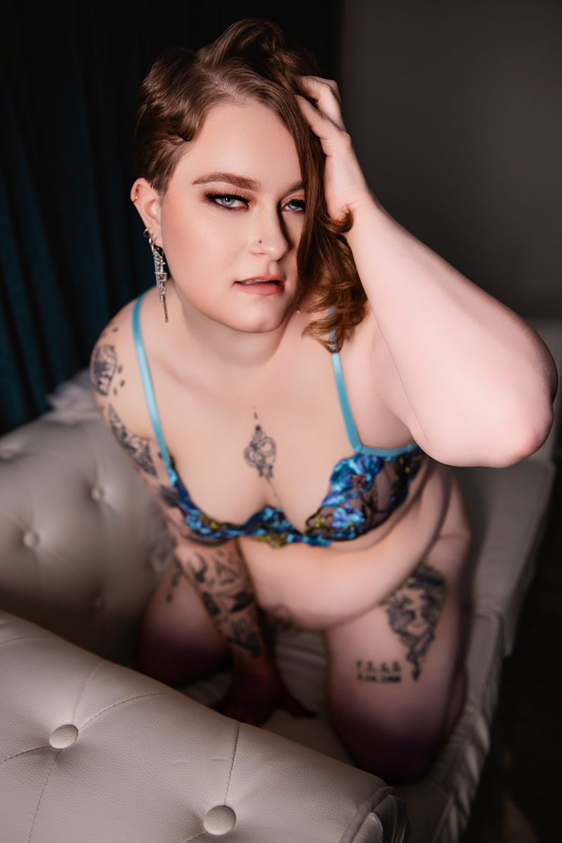A woman kneels on a leather couch with a hand in her hair while wearing blue lingerie after visiting nail salons in indianapolis