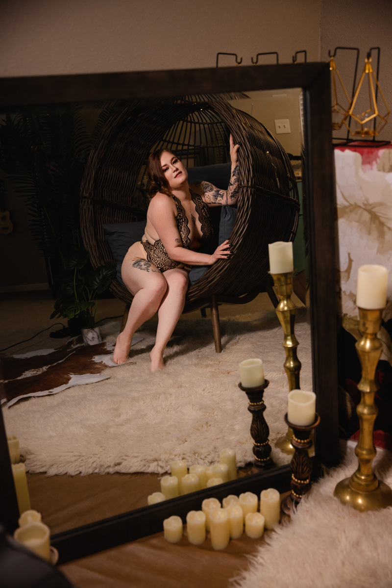 a look into a mirror surrounded by candles at a woman in lace lingerie sitting in a wicker egg chair after visiting nail salons in indianapolis