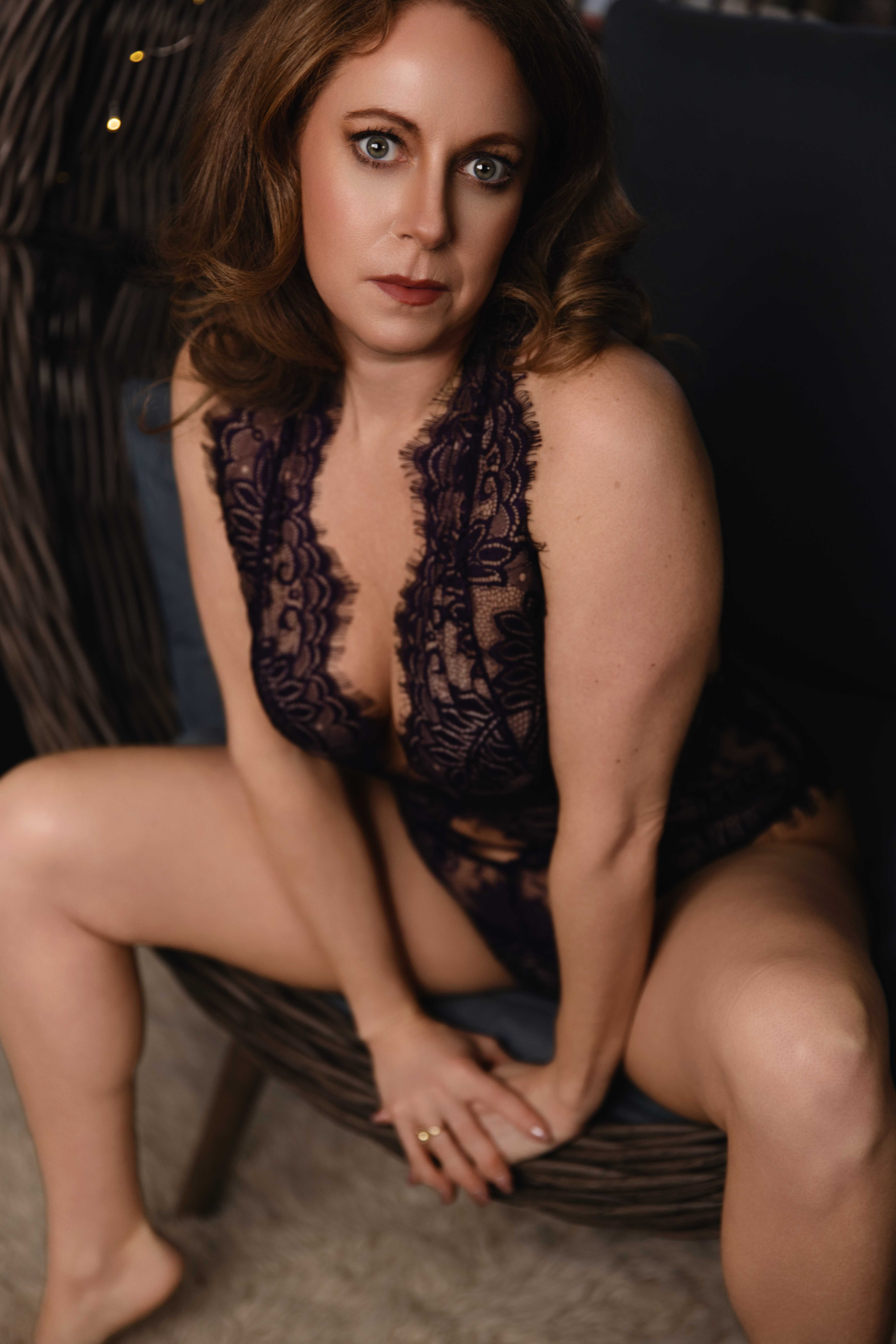 A woman in purple lace lingerie sits with legs spread in a wicker egg chair