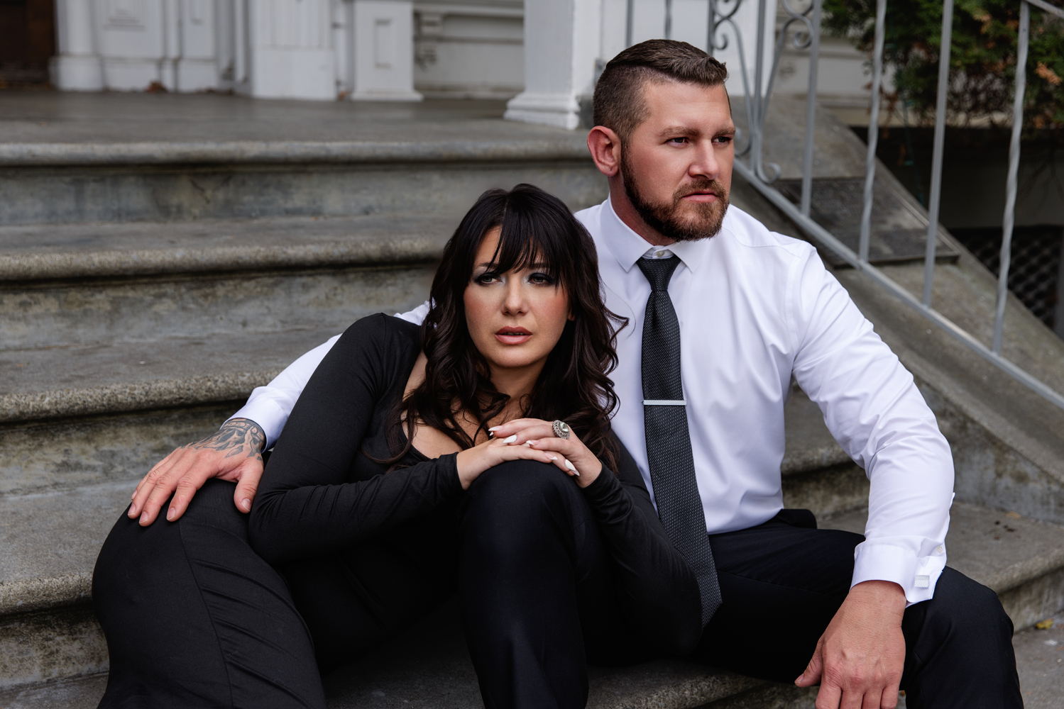 A woman leans in the lap of her partner as they snuggle on a stoop in black and white outfits