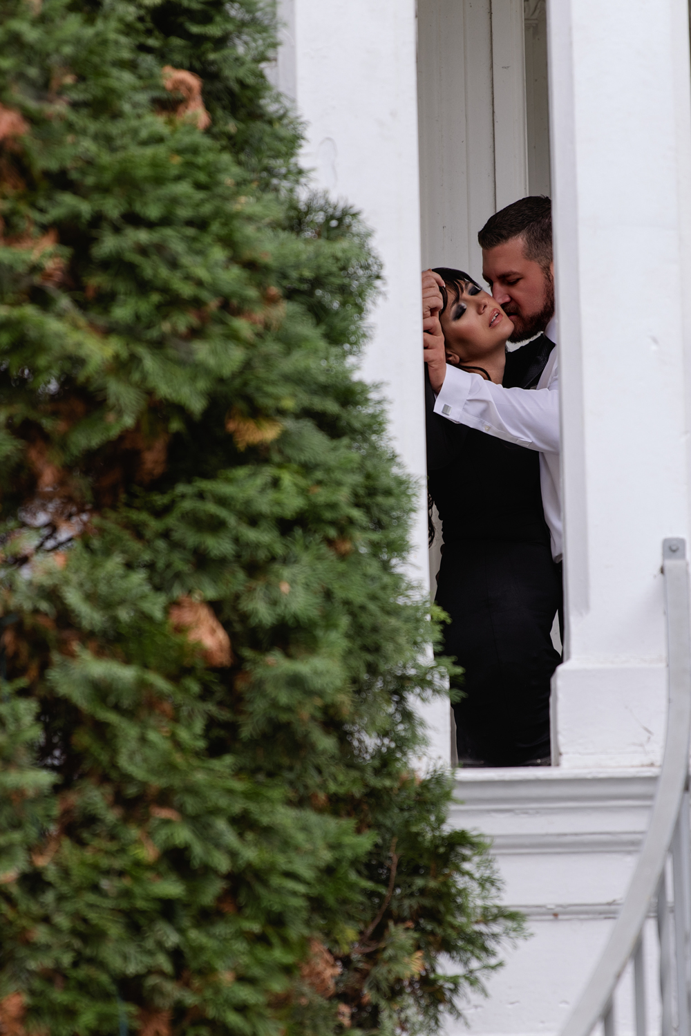 A peek at a couple sharing an intimate moment in black dress and suit behind columns on a porch after visiting romantic restaurants in indianapolis